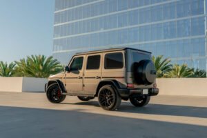 Matte gold Mercedes-AMG G63 from Monza Exotics parked on a rooftop in front of a glass office tower