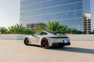 Grey Porsche 911 GTS from Monza Exotics parked on a rooftop in front of a glass office tower